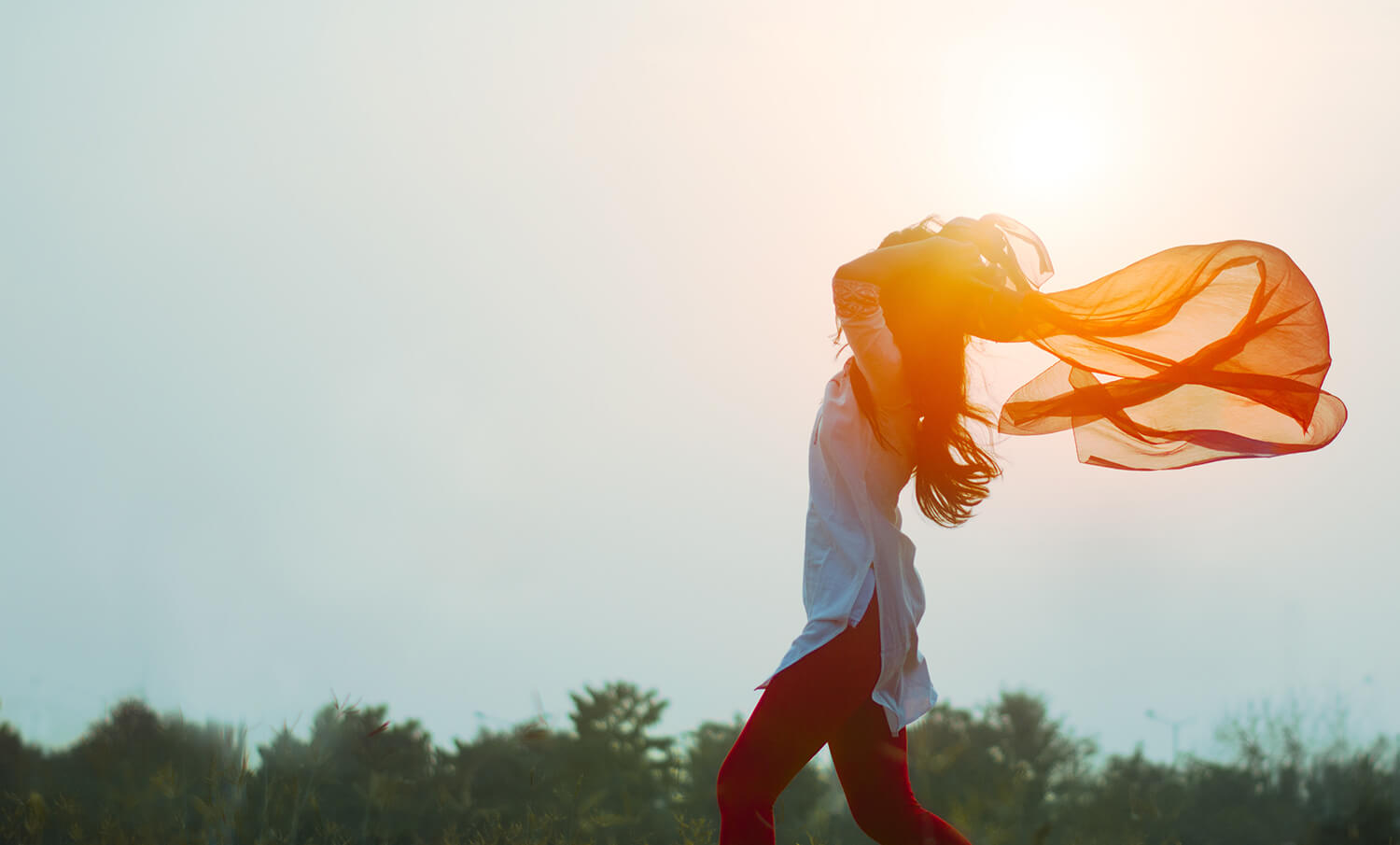 Woman with orange scart blowing above her head in the wind.